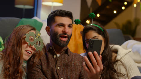 Group-Of-Friends-Dressing-Up-At-Home-Celebrating-At-St-Patrick's-Day-Party-Making-Video-Call-On-Mobile-Phone